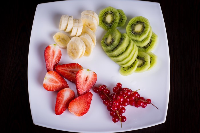 Sliced Fruits on a Plate: Strawberries, Bananas, Kiwi, and Currants