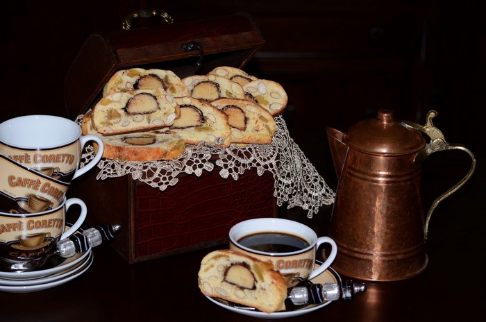 Coffee cups, biscotti, and copper kettle on dark background