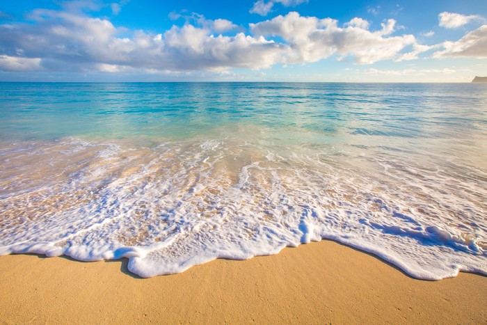 Ocean waves on a sandy beach with clouds and horizon