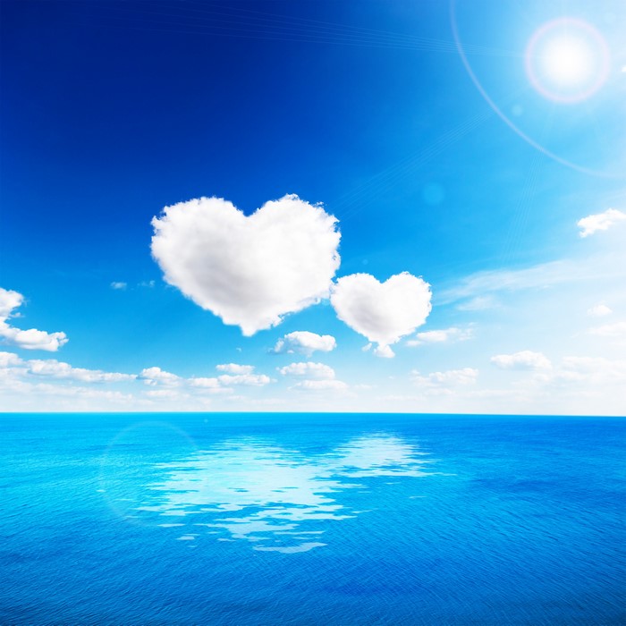 Heart-shaped clouds over the sea under a bright blue sky