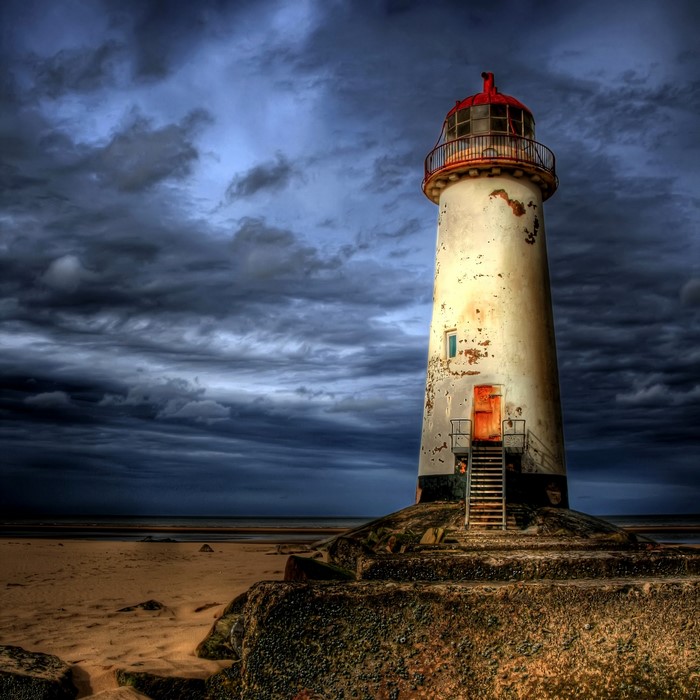 Talacre Lighthouse on a rocky shore under stormy clouds
