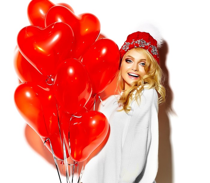 Blonde girl in winter hat with red heart balloons