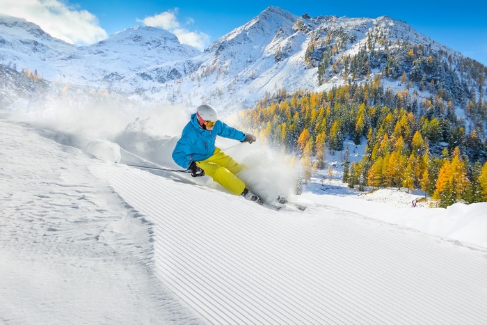 Skiing down a snowy mountain with autumn trees