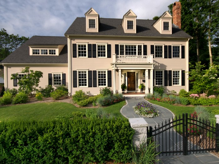 A large beige colonial house with black shutters and a white balcony.