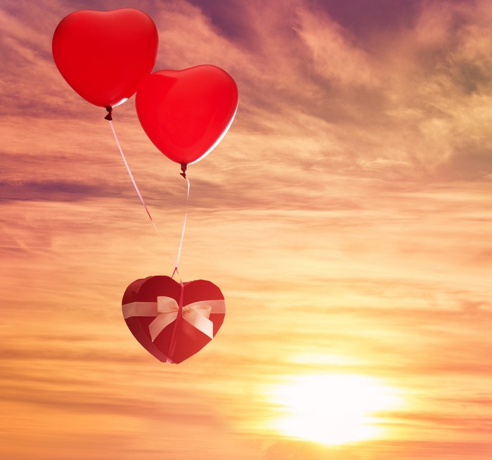 Two red heart balloons carrying a heart-shaped gift box