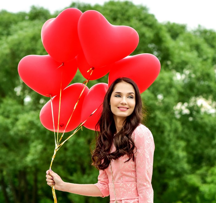 Woman holding red heart balloons outdoors