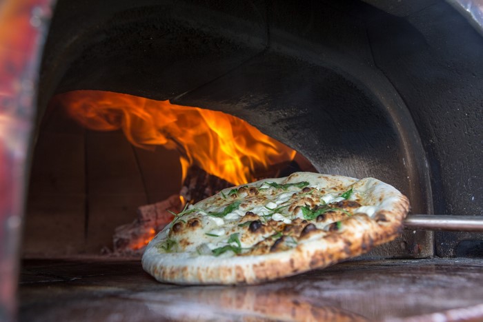 Pizza cooking in a wood-fired oven with flames