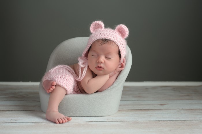 Newborn baby sleeping in a chair wearing a pink hat