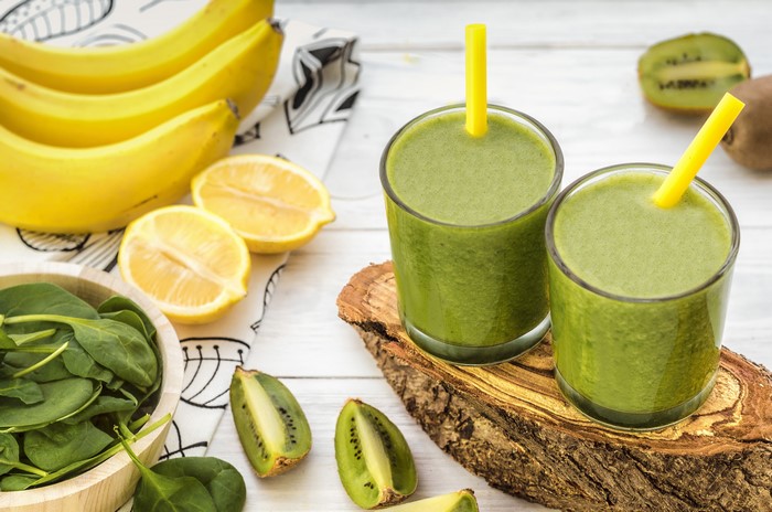 Two glasses of green smoothie with kiwi, bananas, lemons, and spinach