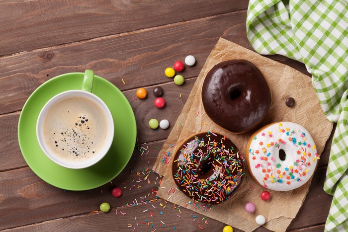 Coffee cup and donuts with candy on wood