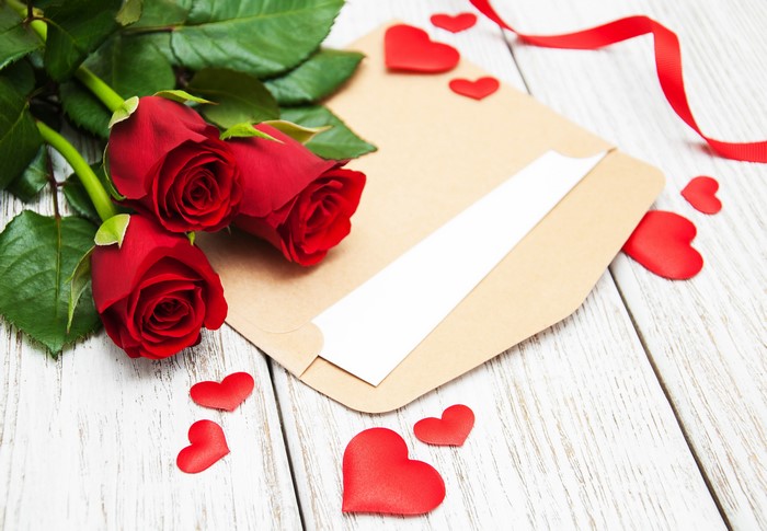 Three red roses on an envelope with hearts and ribbon