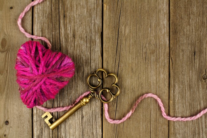 Pink yarn heart and antique key on wood