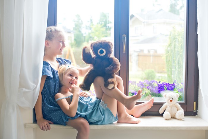 Two little girls with teddy bears by the window