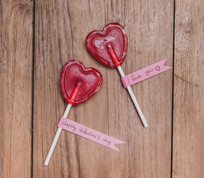 Two heart-shaped lollipops with Valentine's Day messages on wood