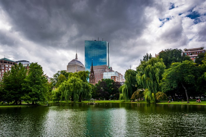 Boston skyline over pond with trees and clouds