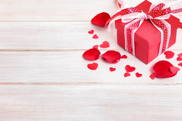 Red gift box with ribbon and rose petals on wood