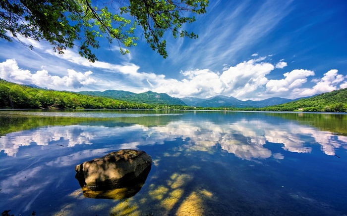 Lake with mountains and trees under a cloudy sky