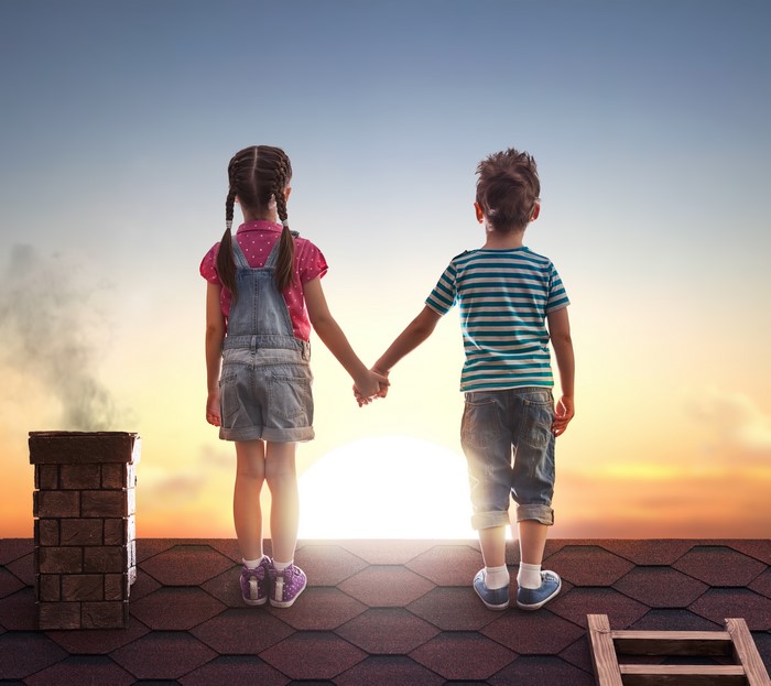 Two children holding hands on a roof at sunset