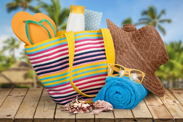 Summer beach bag with flip-flops, hat, sunglasses, towel, and seashells