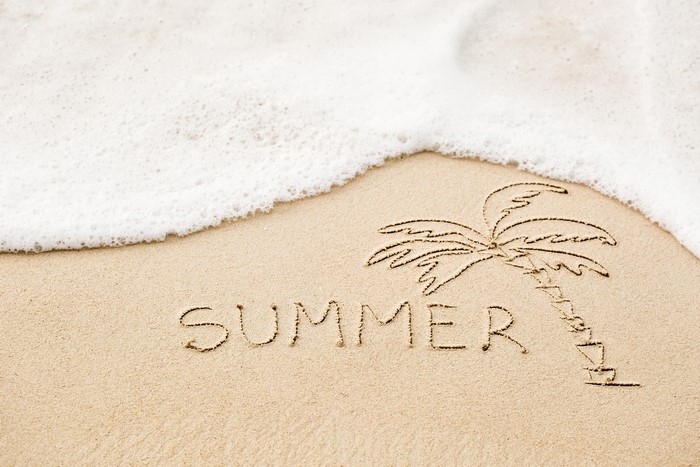 Summer written in sand with a palm tree and wave