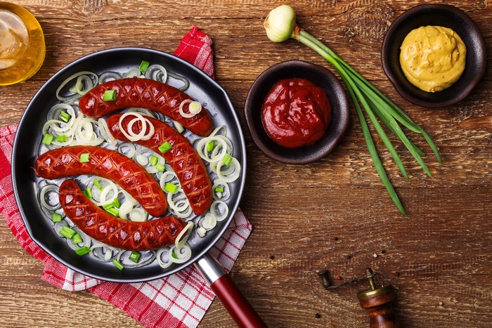 Sausages with onions in a frying pan with ketchup and mustard