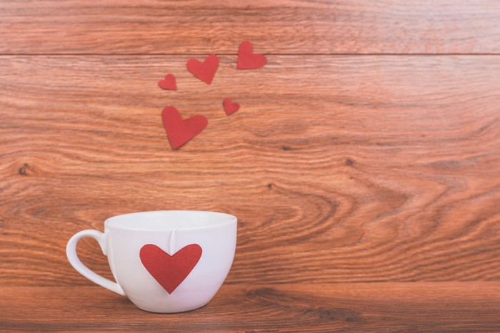 White cup with red heart on wooden background