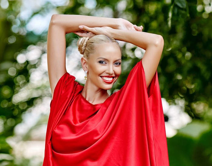 Blonde woman in red dress with hands raised