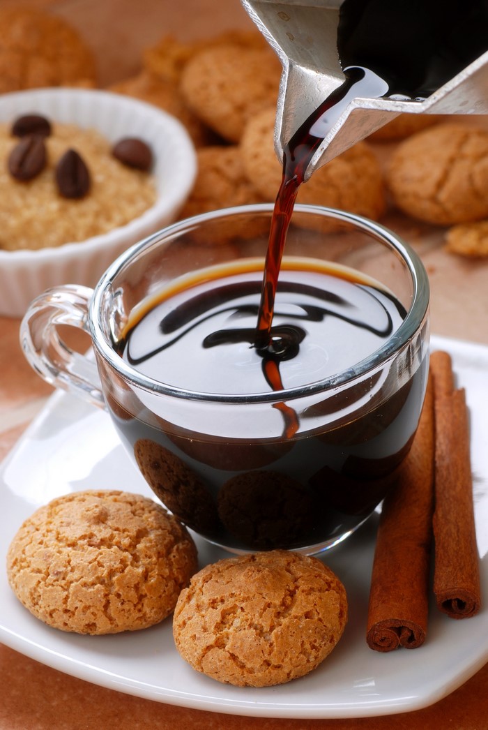 Coffee being poured into a cup with cookies and cinnamon sticks