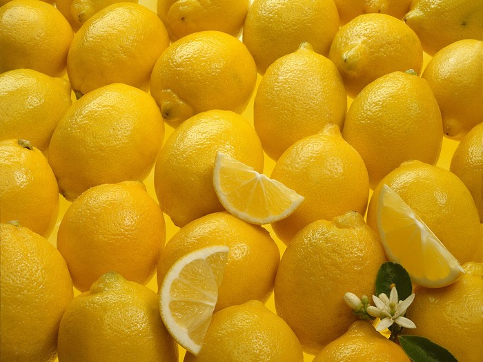 A pile of yellow lemons with slices and a flower
