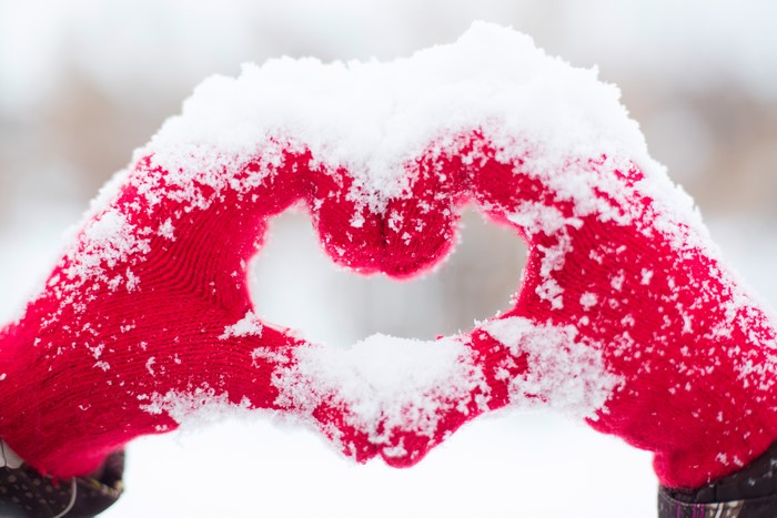 Hands in red gloves forming a heart shape in snow