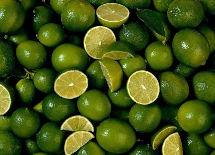 A pile of fresh green limes, some whole and some sliced