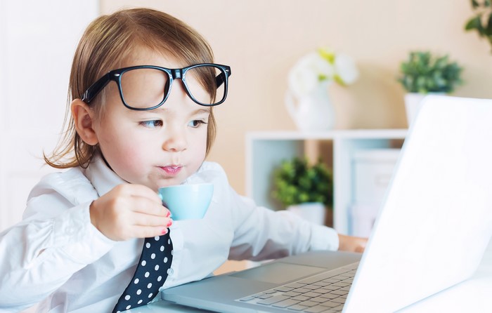 Girl with glasses drinking from cup near laptop