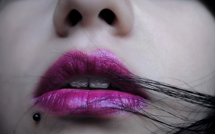 Close-up of woman's lips with pink lipstick and piercing