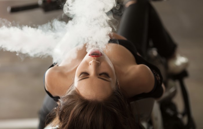 Woman exhaling smoke while lying on a motorcycle