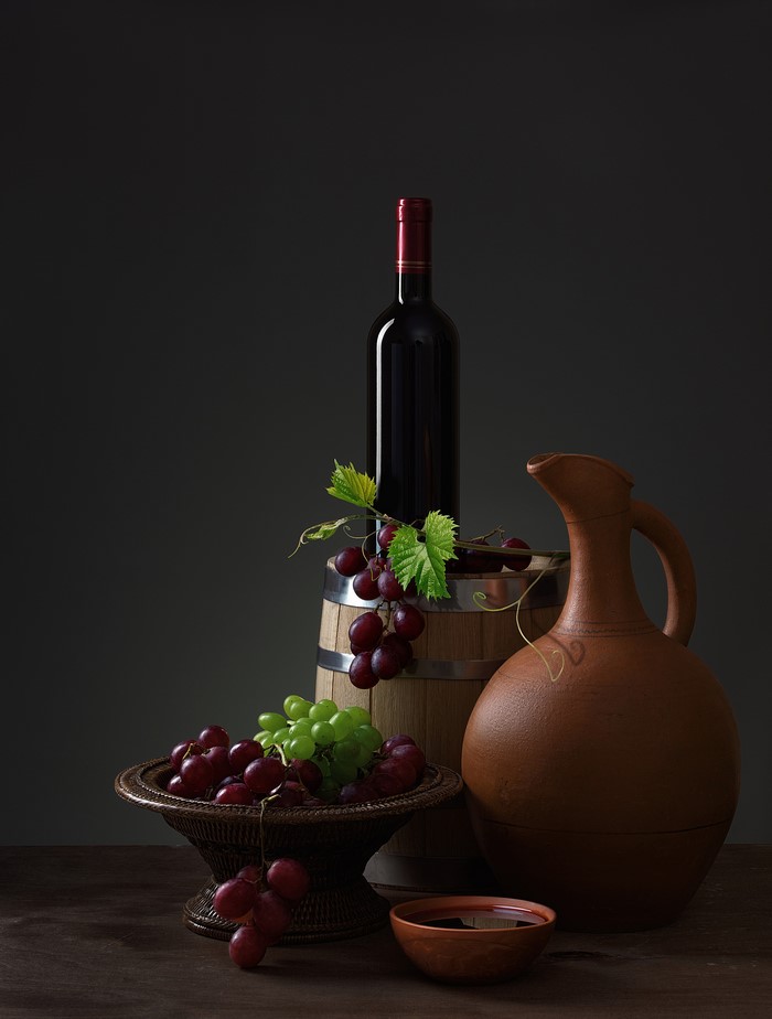 Still life with wine bottle, grapes, barrel, and jug