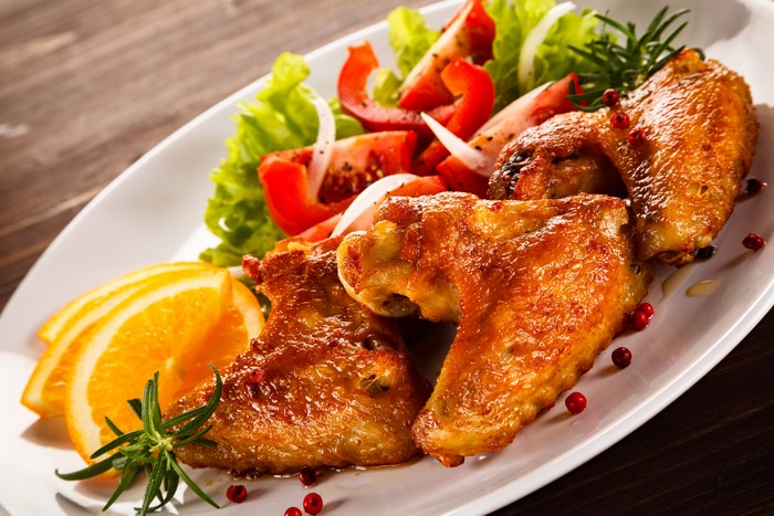Roasted chicken wings with salad and orange slices