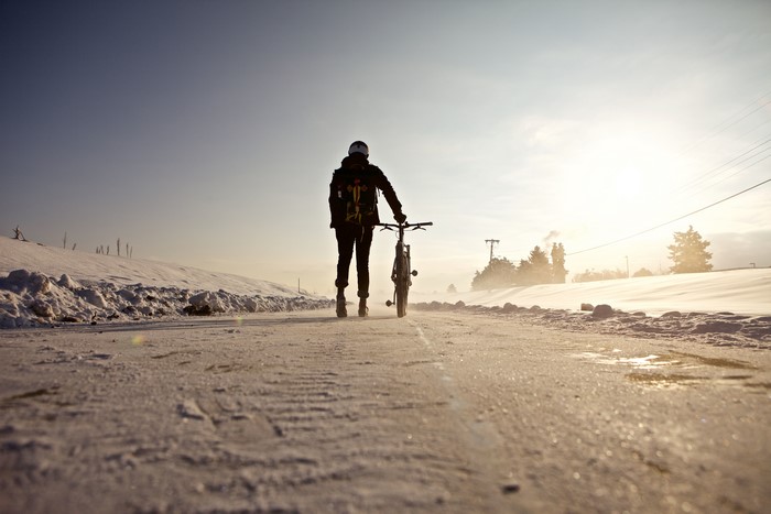Person with bicycle walking on snowy road
