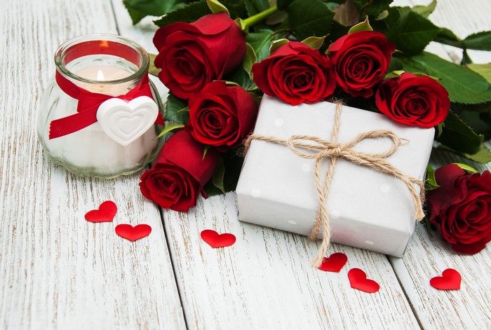 Red roses, candle, and gift on wooden background