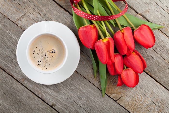 Coffee cup and red tulips on wood planks