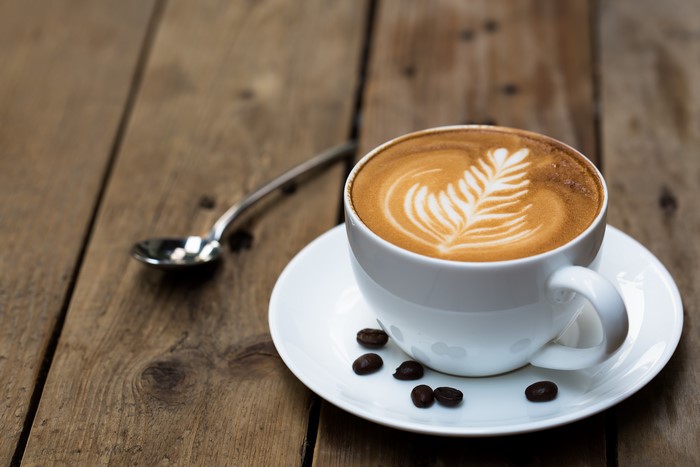 Cappuccino with latte art on a saucer with coffee beans