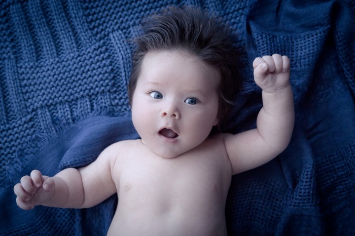 Baby with dark hair and blue eyes on blue blanket