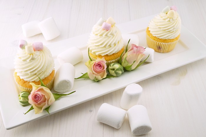 Three cupcakes with frosting, marshmallows, and roses