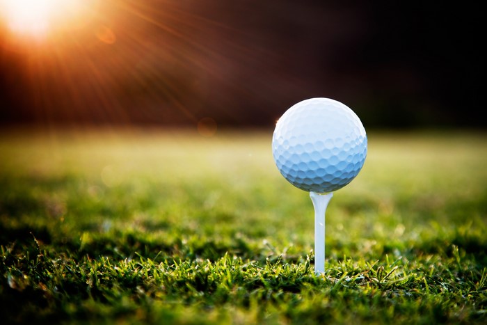Golf ball on a tee in grass with sun flare
