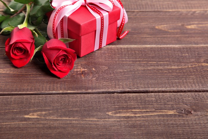 Two red roses and a gift box on wood planks