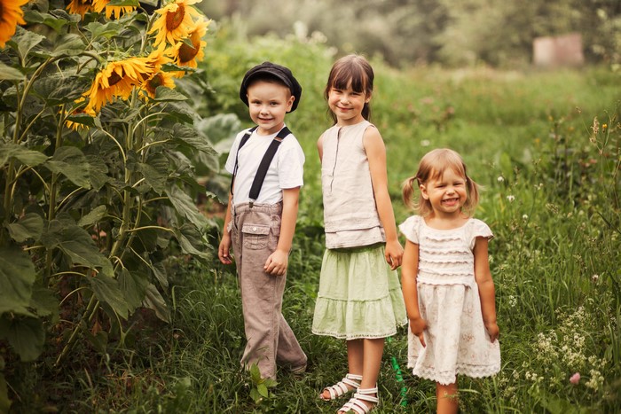 Three children posing by sunflowers