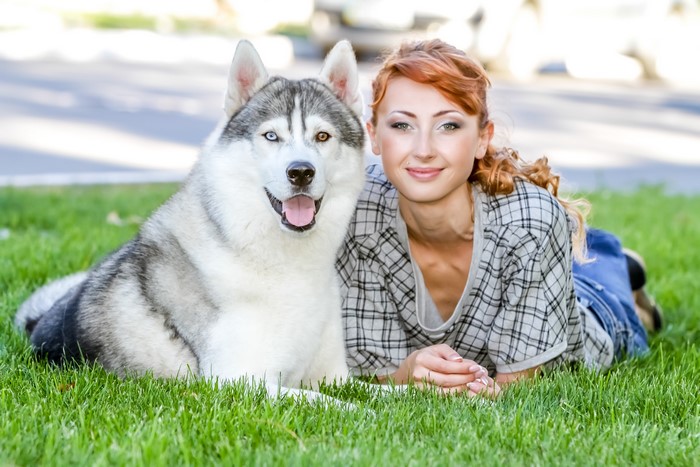 Husky dog and redhead woman lying on grass