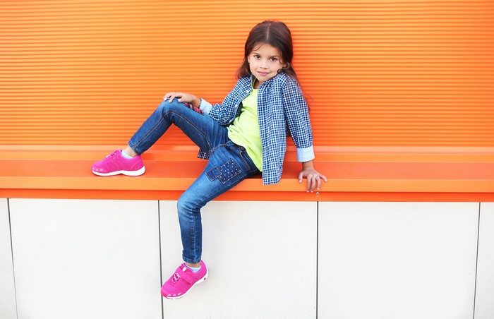 Young girl in jeans and athletic shoes sitting on a bench