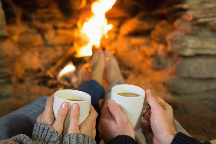 Couple holding mugs by fireplace