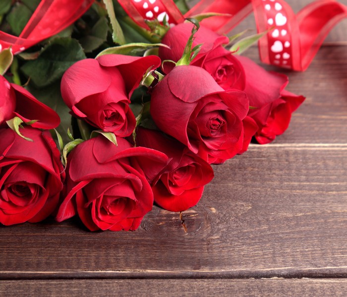 Red roses with ribbon on wooden planks