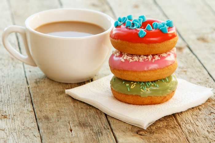 Three donuts and a cup of coffee on wood planks